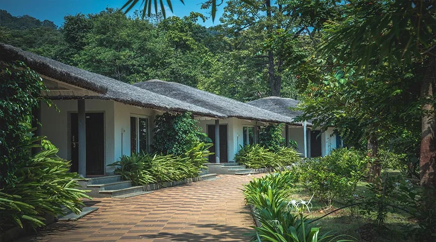 Thatched-roof cottages along a garden path at Whistling Woods Dandeli