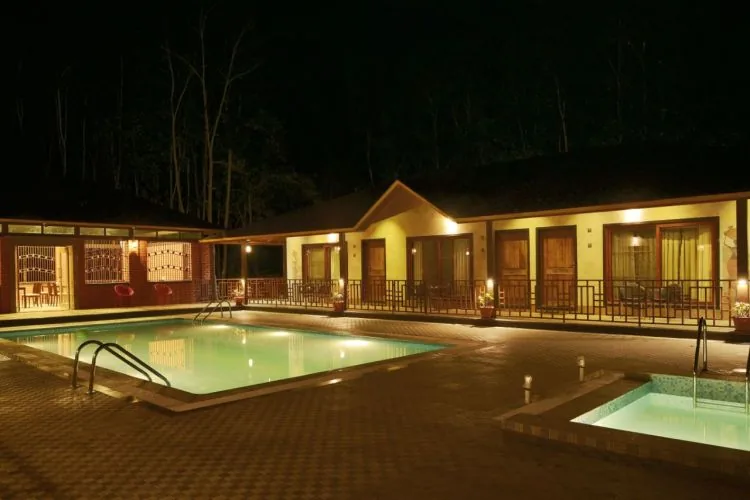 Illuminated pool and guest rooms at night at Dew Drops Resort Dandeli