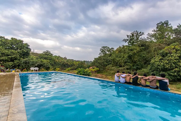 Guests on the pool edge overlooking forest at Tusker Trails Dandeli