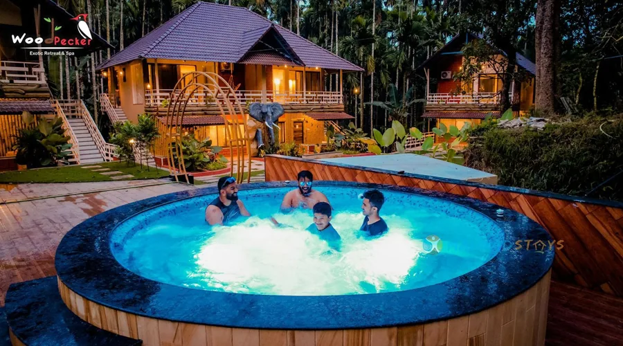 Lit jacuzzi and wooden cottages at dusk at Woodpecker Homestay Dandeli